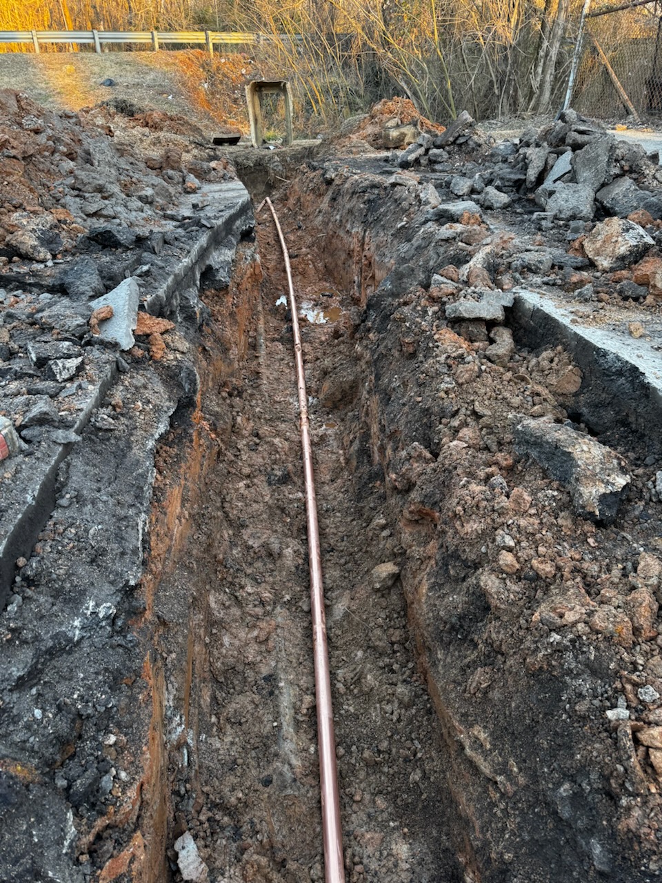 Bravo Plumbing Solutions — new copper water service run through a fresh asphalt-cut trench to the house